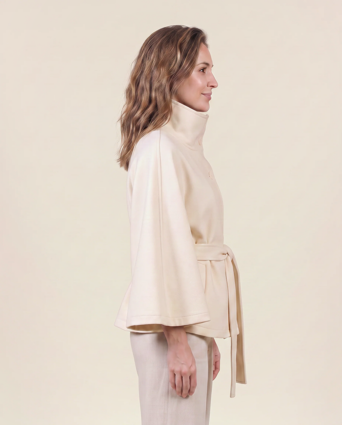 Manteau cape pour femme VELENTI MODA en blanc cassé, à col haut et ceinture nouée, vue de profil.